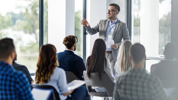 Professional speaker leading a career workshop for a diverse group of young adults seated in a bright, modern room, focused on job readiness and employment skills.